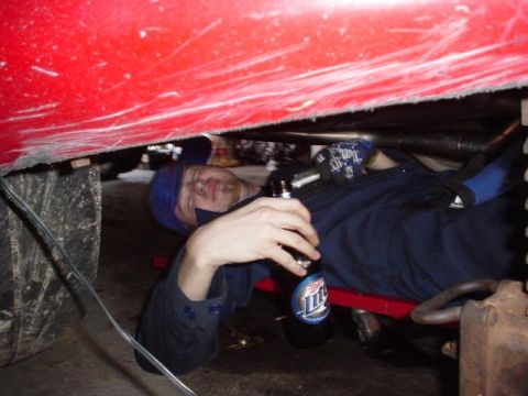 1996 Ford Probe - Mechanic takes a break while working on the underside of a red vehicle.