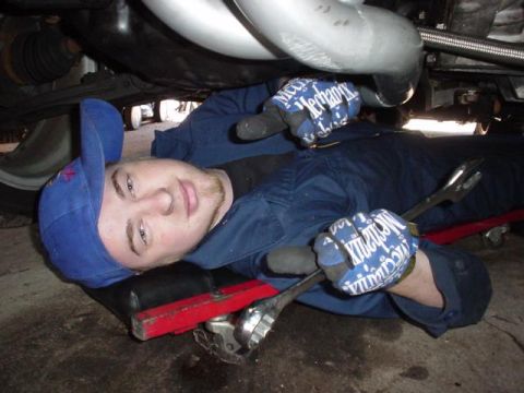 1996 Ford Probe - A mechanic lies on a creeper, working on the exhaust system of a vehicle.