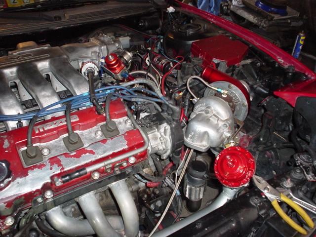 Engine bay with turbocharger, intercooler piping, and red blow-off valve. Wires and hoses are visible