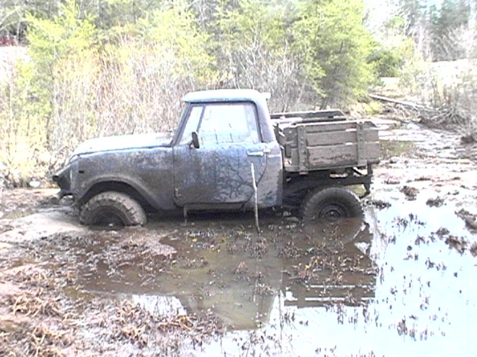 Mud-covered vintage Scout pickup with wood bed stuck in a muddy pond, side view