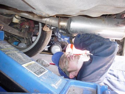 1996 Ford Probe - A mechanic is seen working on the exhaust system of a vehicle, which is raised on a hydraulic jack.