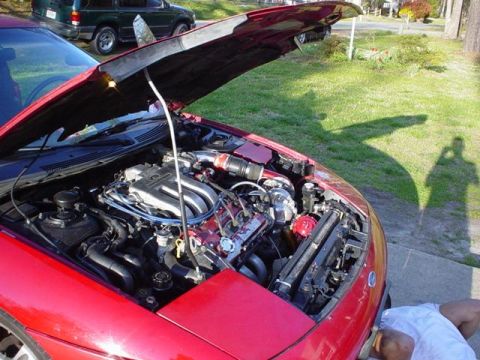 1996 Ford Probe - Engine bay of a red 1996 Ford Probe, with hood raised, revealing the V6 engine and turbocharger.