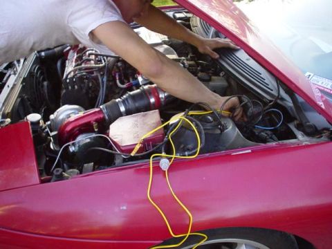 1996 Ford Probe - Mechanic works on the engine bay of a red car, which features a turbocharger and custom wiring.