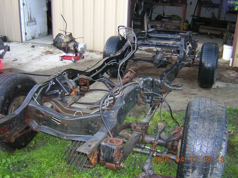 1986 Chevrolet Blazer - The bare frame of a vehicle sits outside a garage with a transmission on a red stand in the background.