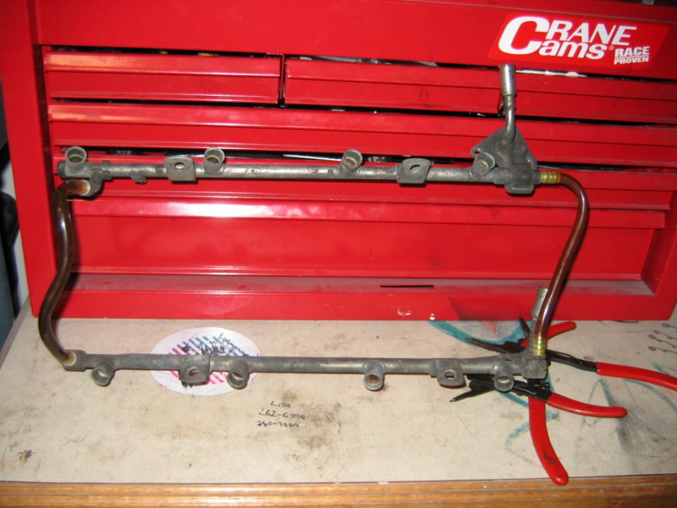 Removed V8 fuel rail assembly on workbench in front of red Crane Cams toolbox