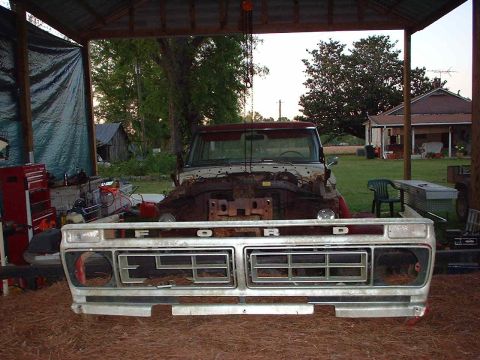 1976 Ford F-150 - The front clip of a Ford truck, including the grille and headlights, is disassembled and stored under a covered area.