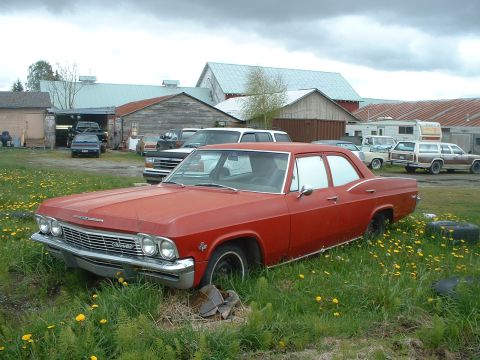 1999 Ford Crown Victoria - This 1965 Chevrolet Impala is parked in a field with other vehicles and farm buildings visible.