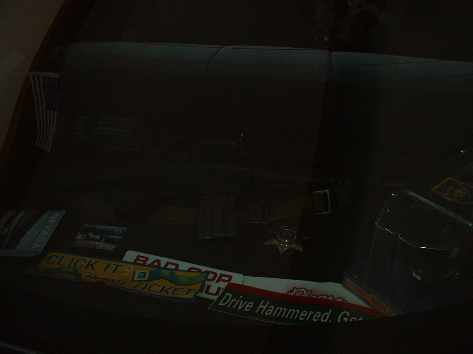Interior shot of car back seat with American flag sticker and various bumper stickers like 'CLICK IT OR TICKET' and 'BAD COP'