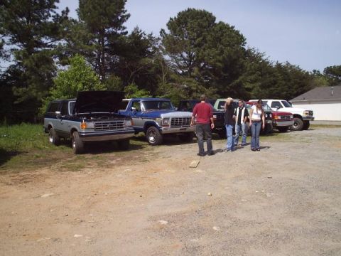 1989 Ford Bronco - Several trucks and SUVs are parked in a gravel lot on a sunny day.