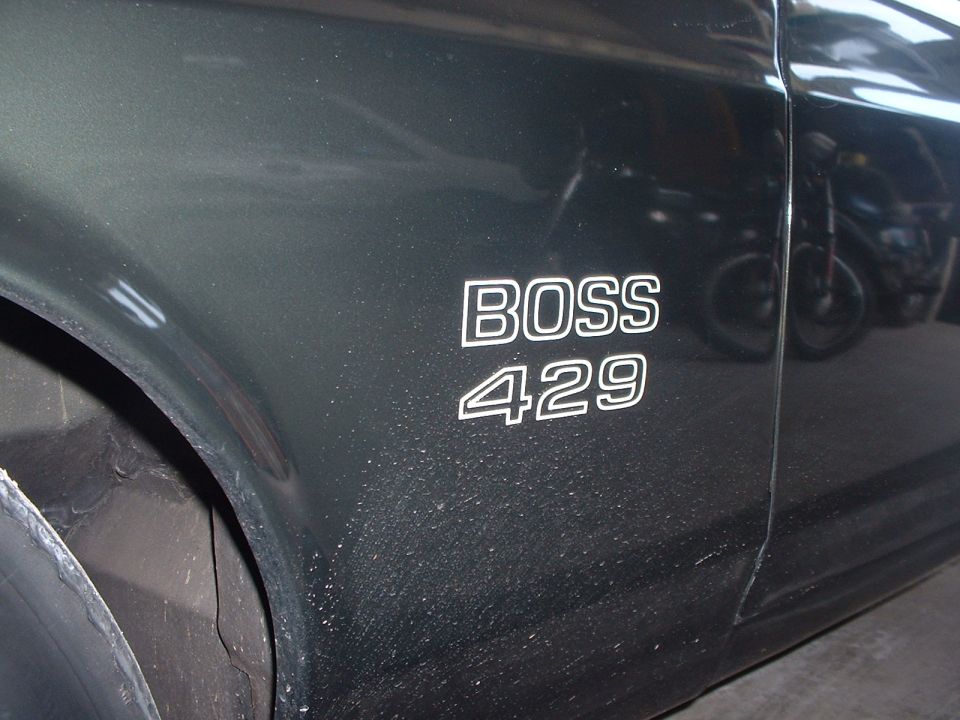 Close-up of 'BOSS 429' emblem on a dark car fender. Motorcycle visible in reflection
