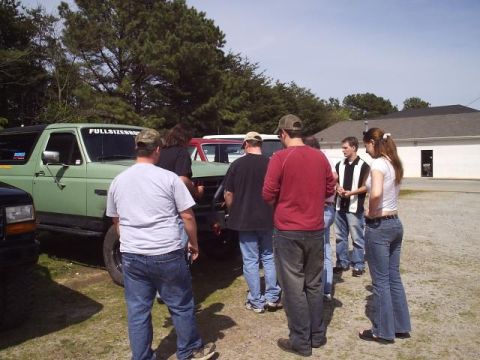 1989 Ford Bronco - A group of people stand around a green Ford Bronco in a parking lot on a sunny day.