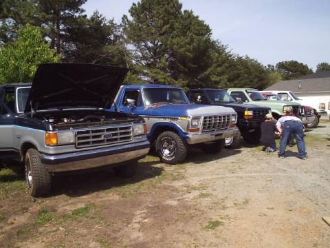 1989 Ford Bronco - Several Ford trucks are parked in a lot, with two people working on one of them.