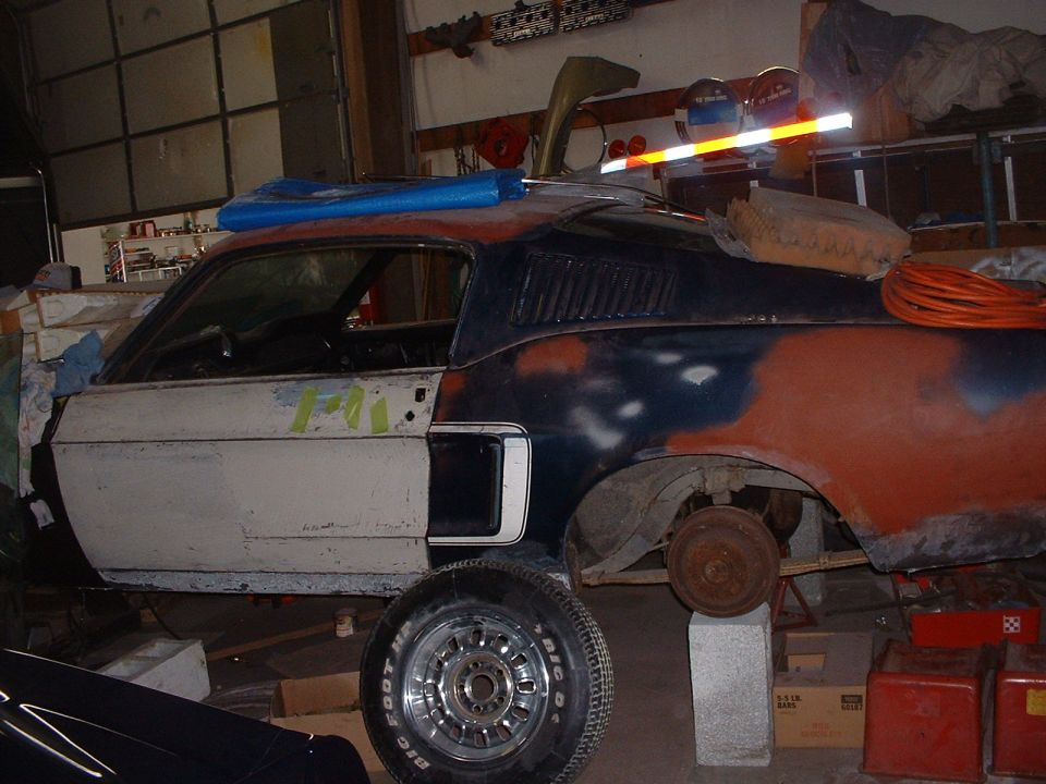 1967 Ford Mustang fastback body in a garage, primer and rust visible, missing wheels
