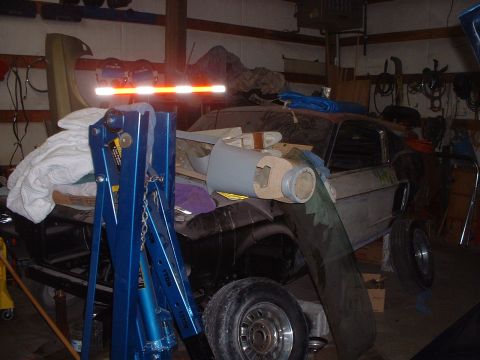 1999 Ford Crown Victoria - A classic Ford Mustang is stored in a cluttered garage, surrounded by car parts and equipment.