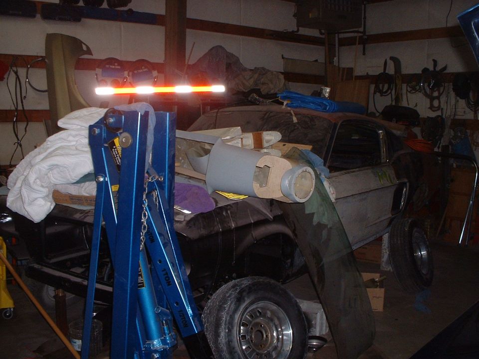 Old Ford Mustang in garage with engine hoist and parts around it