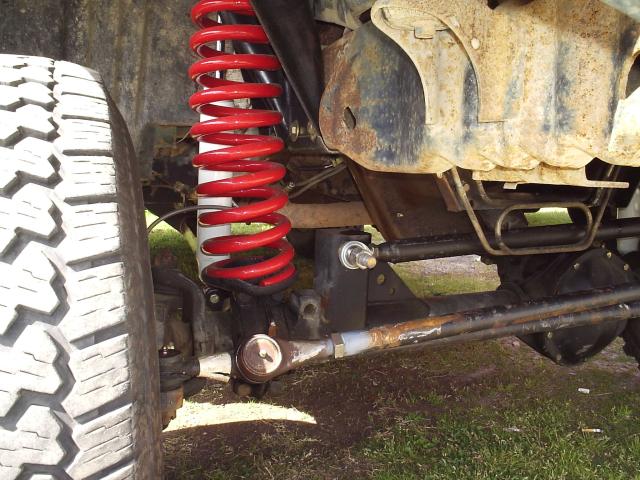 Red coil spring, radius arm bracket and tie rod on a solid front axle seen from below