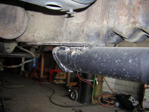Underside view of a vehicle showing driveshaft and transmission crossmember in a garage