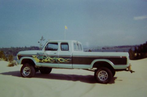 1994 Ford F-150 - A lifted, custom-painted crew cab pickup truck is parked on a sandy surface under a clear blue sky.