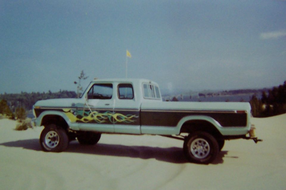 Light blue and dark brown crew cab pickup truck with flame decals, lifted suspension, and aftermarket wheels