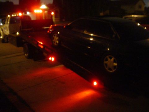 1993 Ford Taurus - A dark sedan is loaded onto a tow truck at night, illuminated by red lights.