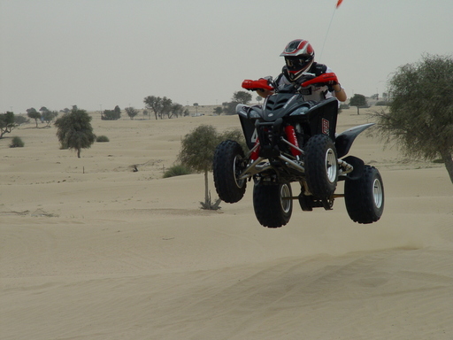 Black quad ATV with red rider jumping over desert sand dunes