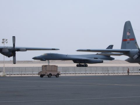1988 Ford Bronco - A B-1 Lancer bomber is parked on the tarmac near a C-130 Hercules aircraft, with a small utility cart nearby.