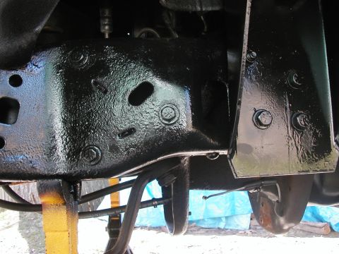 1994 Ford Bronco - Close-up from underneath a truck showing a freshly black-painted front frame crossmember, bolted brackets and a skid plate, with a routed b…