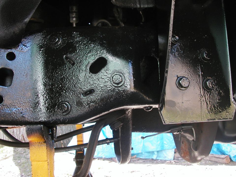 Underside close-up of black-painted truck frame crossmember and brackets