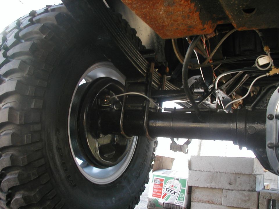 Close-up of a vehicle's rear axle, leaf springs, and tire. A box of Castrol GTX is visible