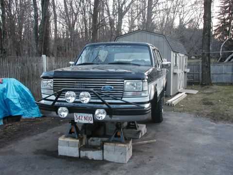 1994 Ford Bronco - A black 1994 Ford Bronco is elevated on jack stands, an aftermarket bumper with auxiliary lights.