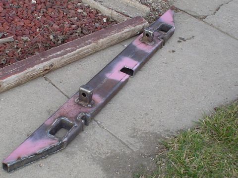 1981 Ford Bronco - A shop-built tubular steel bumper lying on a concrete driveway, blotched with pink primer and bare grinder-cleaned weld seams. It carries t…