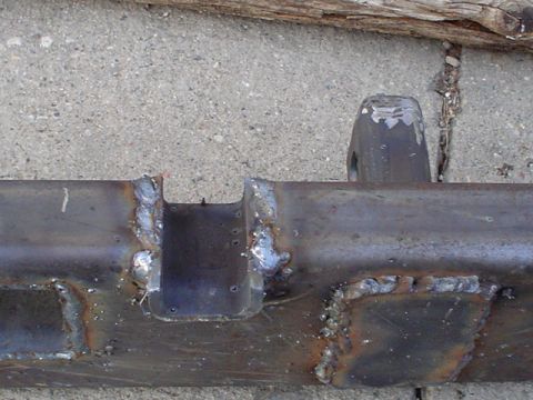 1981 Ford Bronco - Tight shot of the welded center section of a shop-built steel bumper on a concrete driveway, showing a notched channel gusset and square sh…