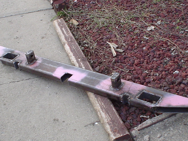Fabricated steel bumper in pink primer with shackle slots and tabs on a driveway