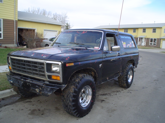Black lifted 1980s Ford Bronco on mud tires and chrome wheels parked on a street by townhouses