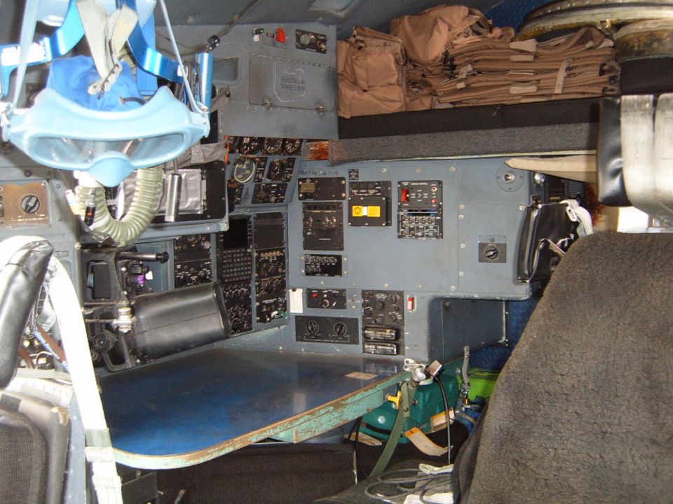 Cockpit with lots of buttons and screens, plus a harness hanging down