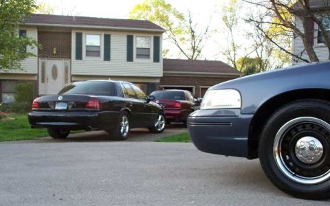 1998 Ford Crown Victoria - Two Ford Crown Victorias are parked in front of a suburban house.