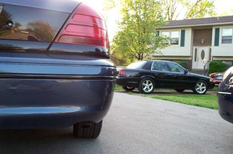 1998 Ford Crown Victoria - A dark blue sedan is parked in the foreground, with a black sedan visible in the background.