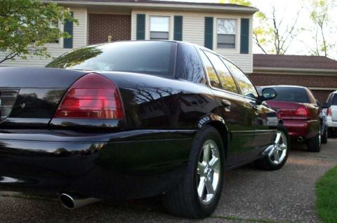 1998 Ford Crown Victoria - A black 1998 Ford Crown Victoria is parked in a driveway, showing off its chrome wheels and rear end.