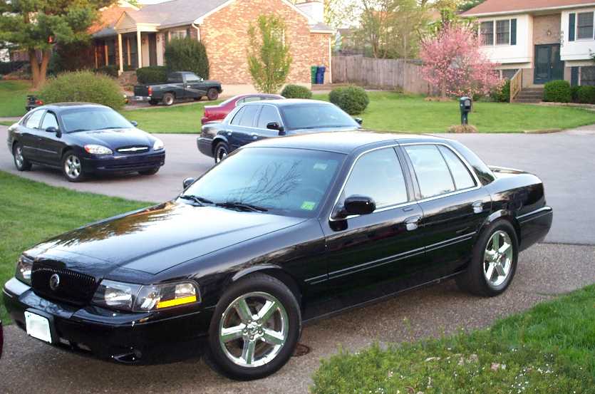 Black full-size sedan with chrome wheels parked in a suburban driveway, front-three-quarter view