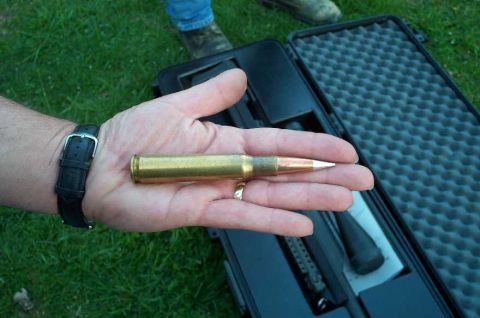 1998 Ford Crown Victoria - A large ammunition cartridge is held in a hand, with a protective case visible in the background.