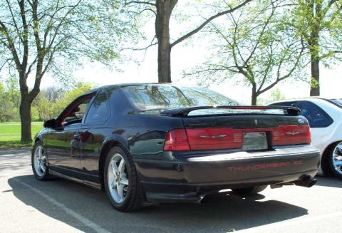 1998 Ford Crown Victoria - A dark green Ford Thunderbird SC coupe shown from the rear three-quarter angle, with aftermarket polished five-spoke wheels, full-width tai…