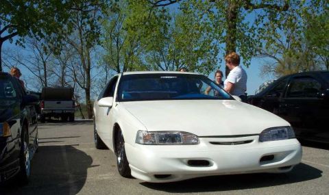 1998 Ford Crown Victoria - A white two-door coupe, likely a 1990s Ford Thunderbird, is parked in a lot with a lowered stance and aftermarket wheels, its front and sid…