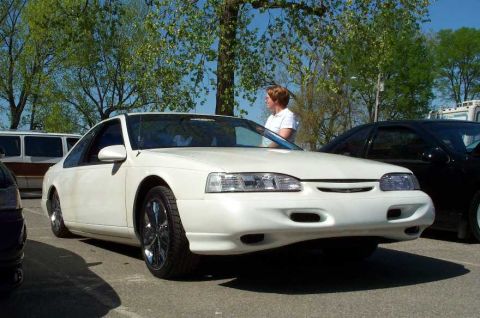 1998 Ford Crown Victoria - A white two-door coupe photographed from the front-three-quarter angle, lowered on chrome multi-spoke wheels with low-profile tires, parked…