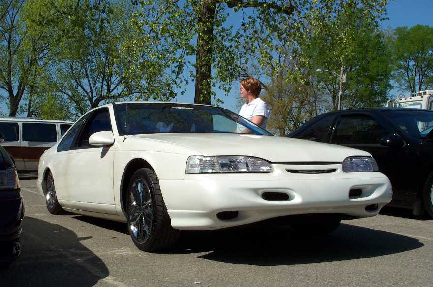 White lowered coupe on chrome wheels, front 3/4 view in a parking lot
