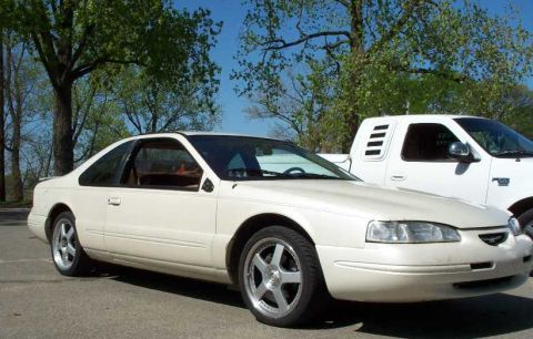 1998 Ford Crown Victoria - A cream/white two-door coupe photographed from a front three-quarter angle, with polished multi-spoke alloy wheels and a rounded 1990s body…
