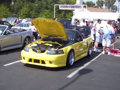 2002 Ford Mustang - A yellow convertible Mustang is displayed with its hood open at an outdoor car show.