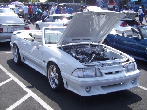 2002 Ford Mustang - A white convertible with its hood open is displayed at an outdoor car show.