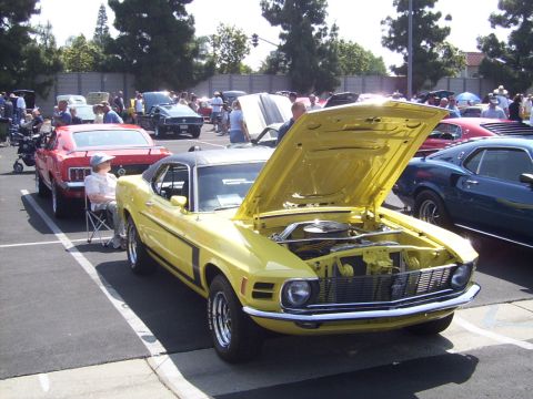 2002 Ford Mustang - A yellow 1970 Ford Mustang is displayed with its hood open at an outdoor car show, alongside other classic vehicles.