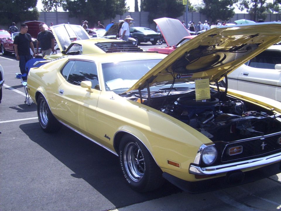 Yellow 1971 Ford Mustang coupe with hood open, parked at an outdoor car show