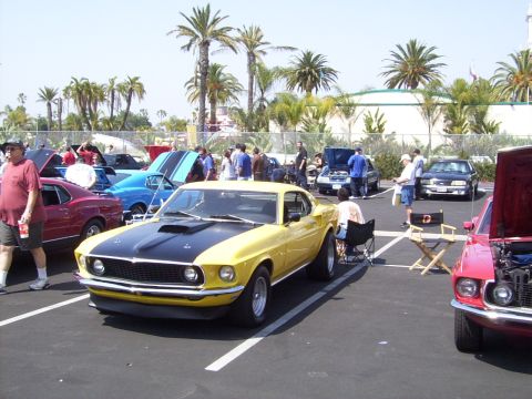 2002 Ford Mustang - A yellow and black classic Mustang is parked at a car show with other vehicles and people around.